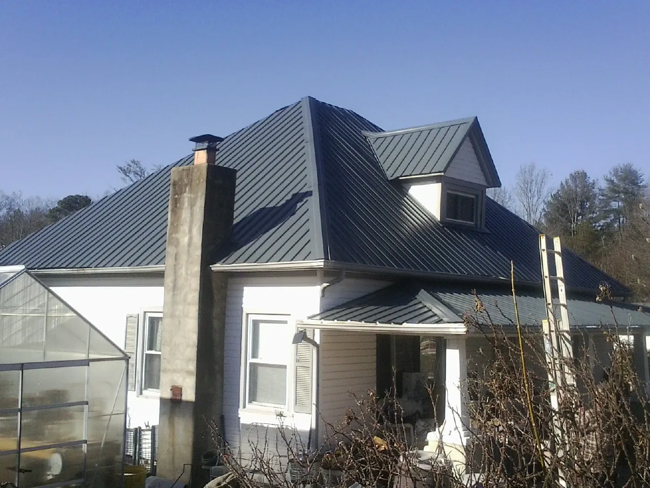 Dark blue standing seam metal roof on a white farmhouse with dormer — Slate & Tile Roof Repair by Roofing Brothers in Joanna