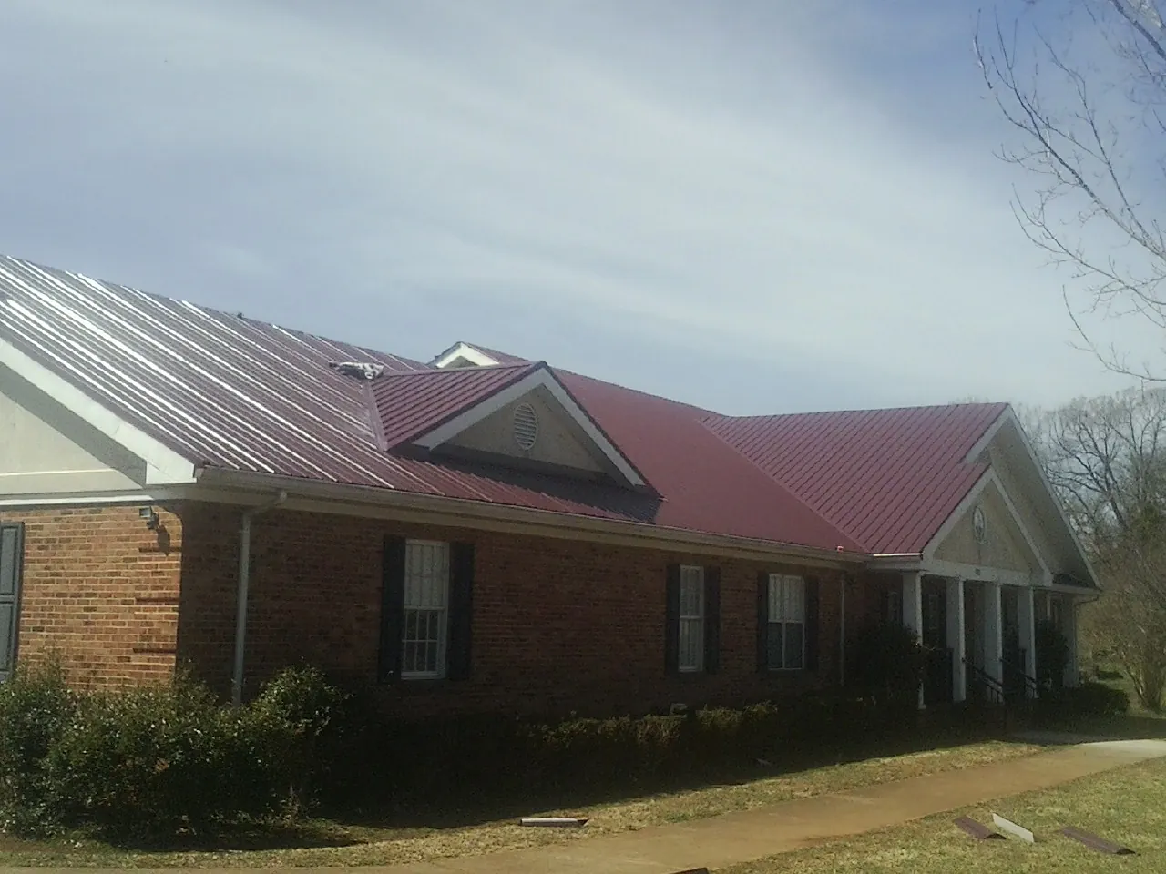 Red metal roof with gabled entries on a long brick building, from a Hail Damage Roof Repair job in Joanna