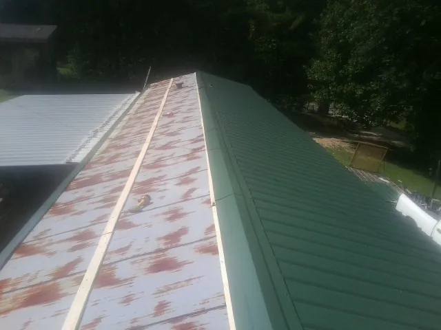Old rusted panels beside newly installed green metal roofing — Wind Damage Roof Repair by Roofing Brothers in Joanna
