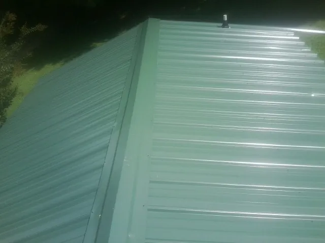 New green metal panels meeting at the ridge of a roof — Flat Roof Repair work by our crew in Joanna