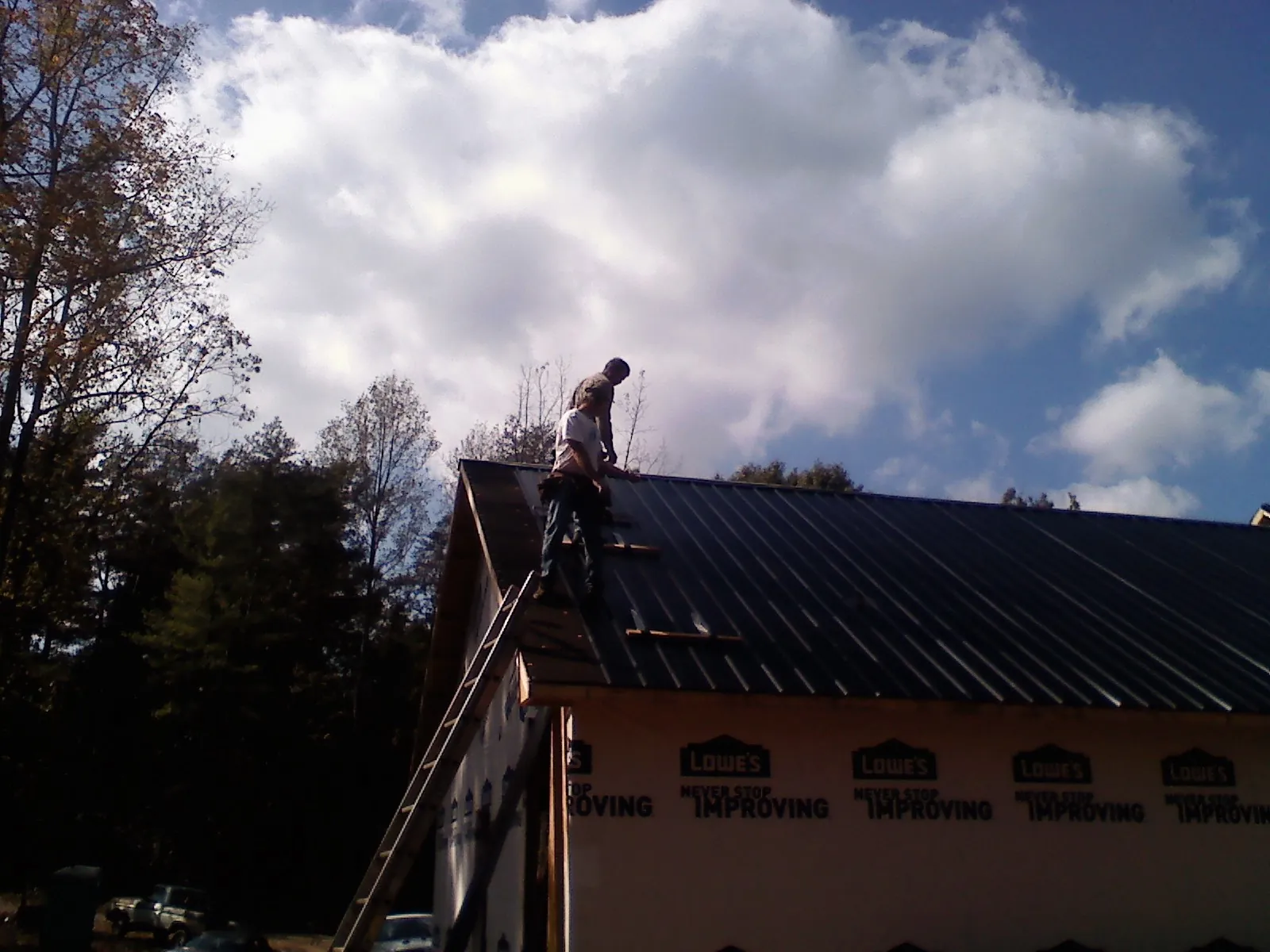 Roofer fastening dark metal panels high against a cloudy sky, from a Roof Inspection job in Joanna