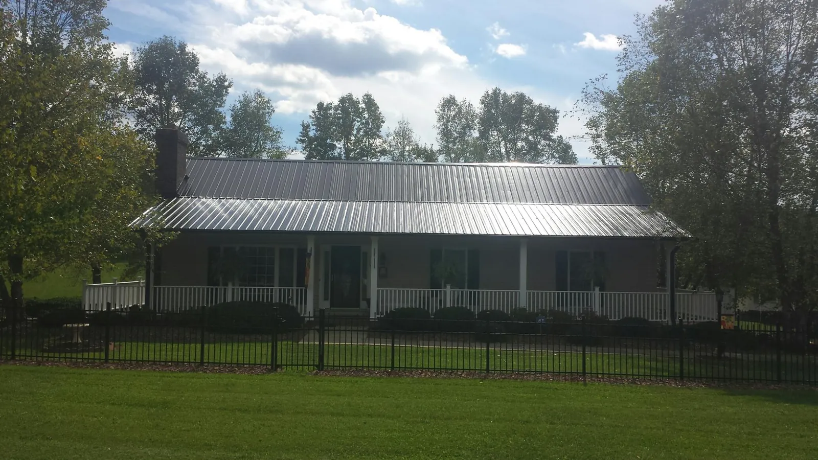 Gray metal roof on a brick ranch with a full width front porch — Gutter Guard Installation work by our crew in Joanna